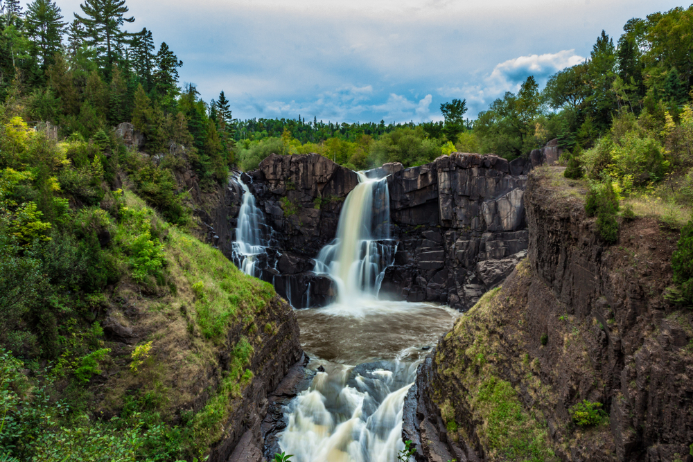 High Falls Waterfall. Rocks with water pouring over them and trees all around the top. Things to do in Grand Marais MN