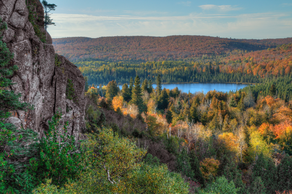 View over Oberg Mountain with a rock in the foreground, tress and fall foliage and a lake in the background.