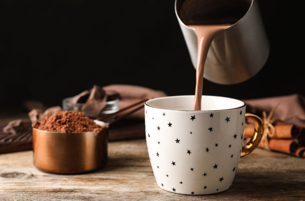 Hot chocolate been poured into a cup with stars on and cocoa powder besides it.