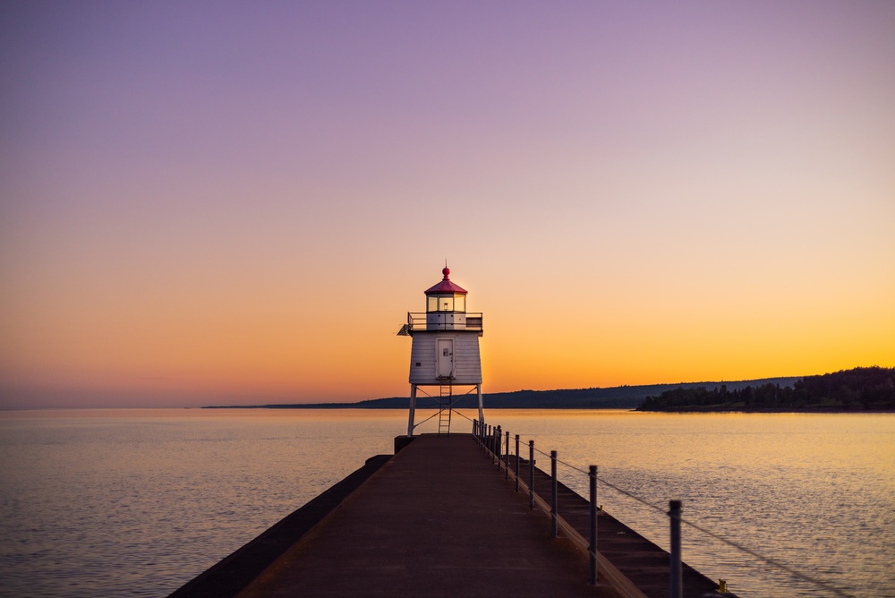 Lighthouse in Grand Marais, Minnesota at sunset in shadowy light on Lake Superior with a colorful purple, blue, and orange sky. The article is about things to do in Grand Marais MN