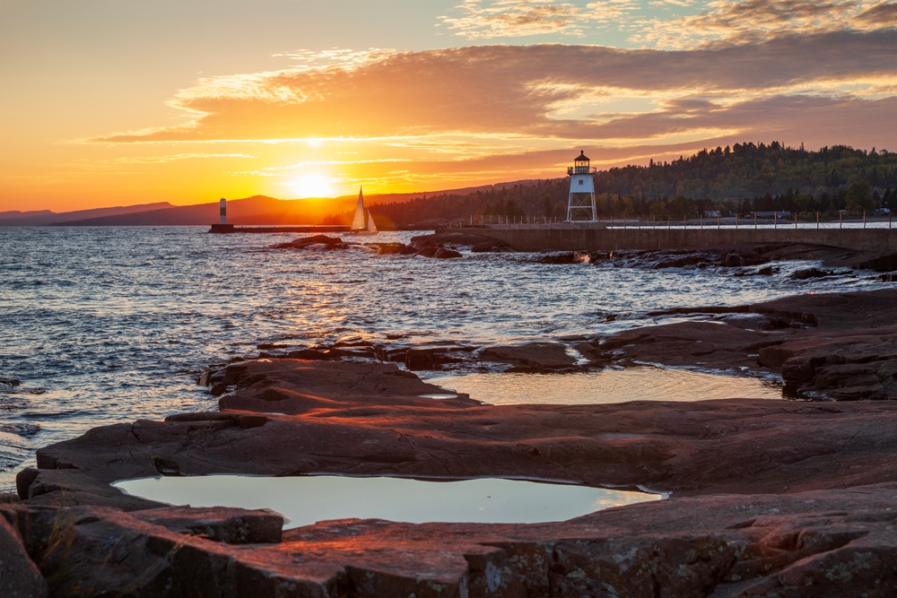 Sailboat entering the harbor at Grand Marais viewed from Artist's Point at sunset on an autumn day. The article is about things to do in Grand Marais MN