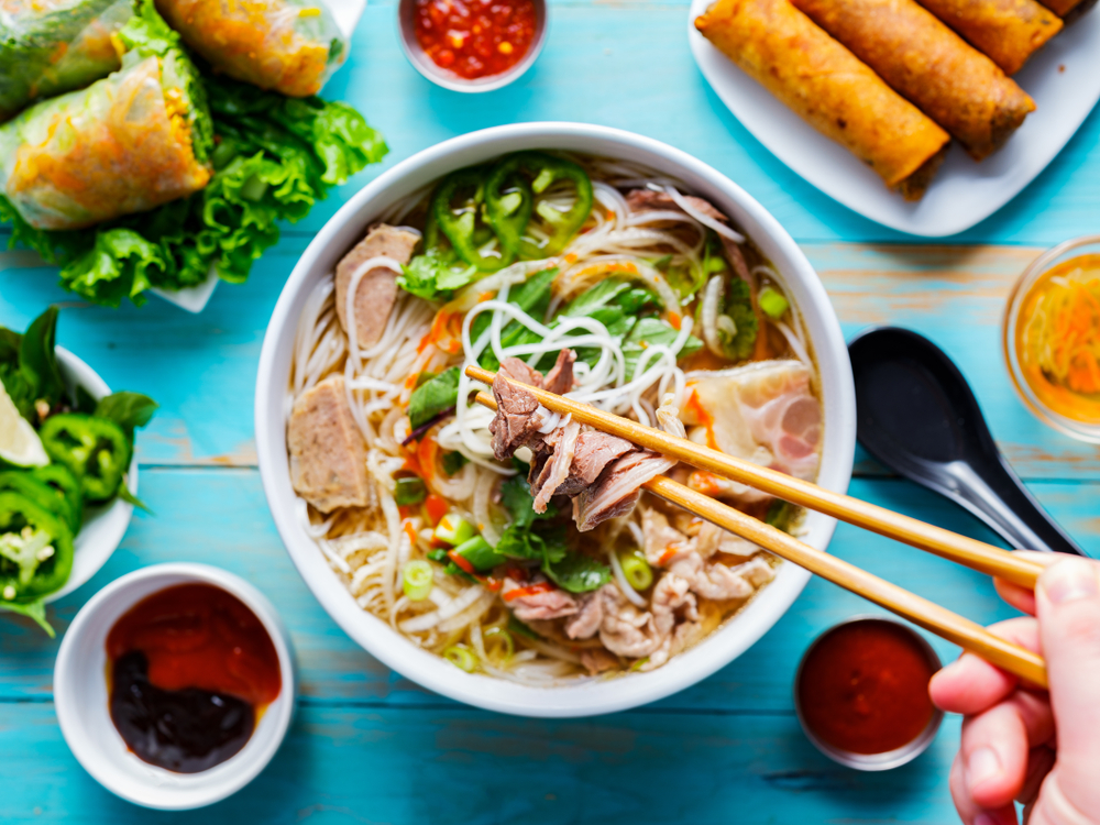 Bowl of pho surrounded by spring rolls and dips.