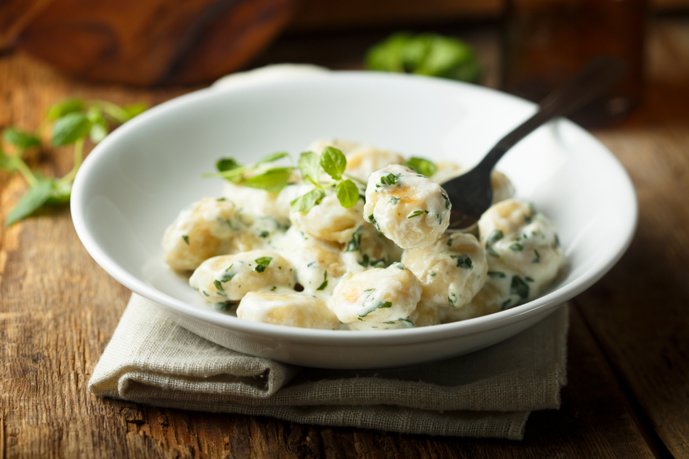 Gnocchi with herbs in a white bowl on brown wooden table. At an upscale Des Moines IA restaurant.