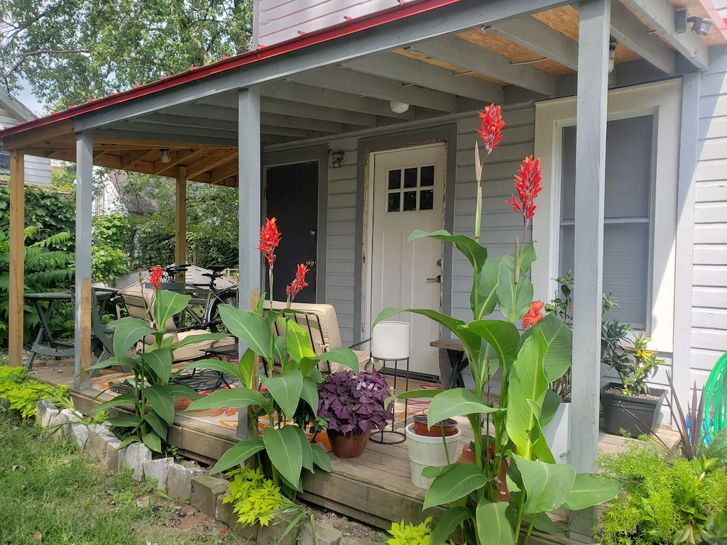 Charming grey cottage with white front door, patio, and blooming flowers in foreground.