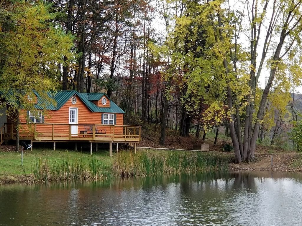 Log cabin with green roof and wooden balcony/railing sits right next to tranquil lake VRBO in Ohio