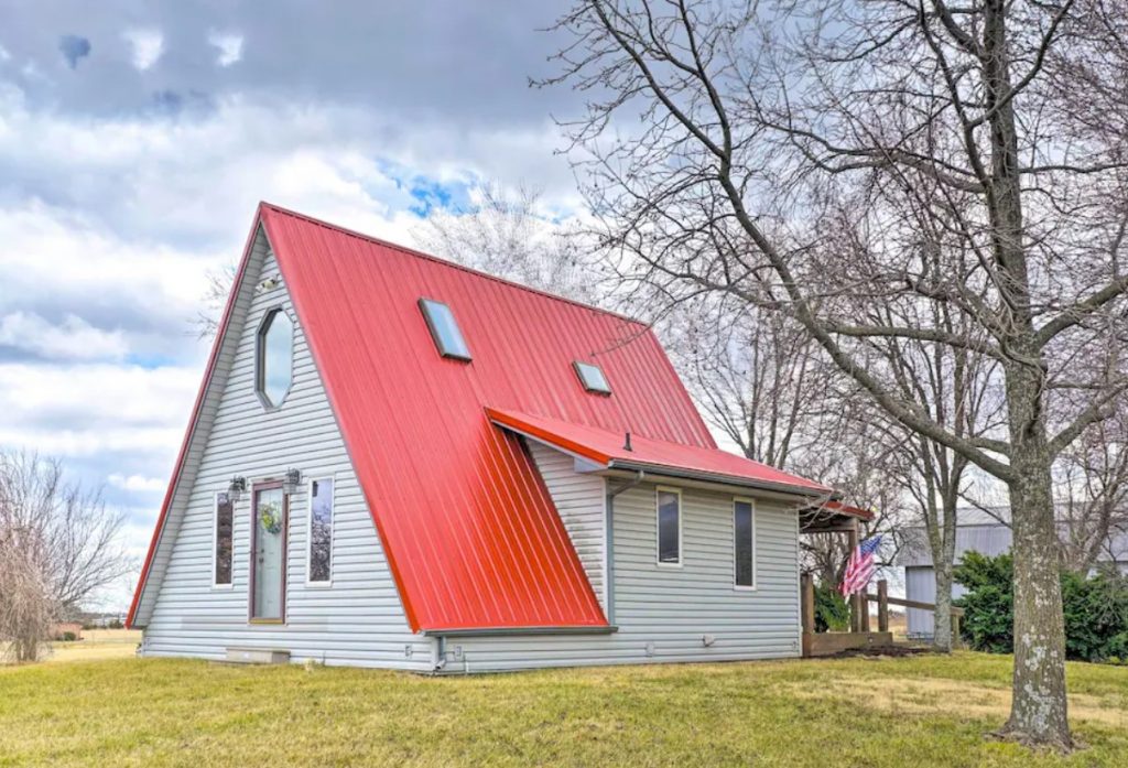 A-frame cabin with red metal roof, white plank exterior, tall thin windows and green grass in foreground.
Midwest cabins