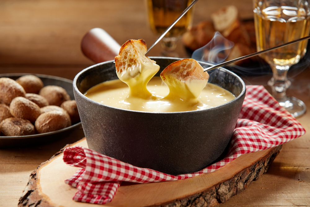 Cheese in black bowl with skewers holding bread cubes dipping into it at one of the best Restaurants in Des Moines.