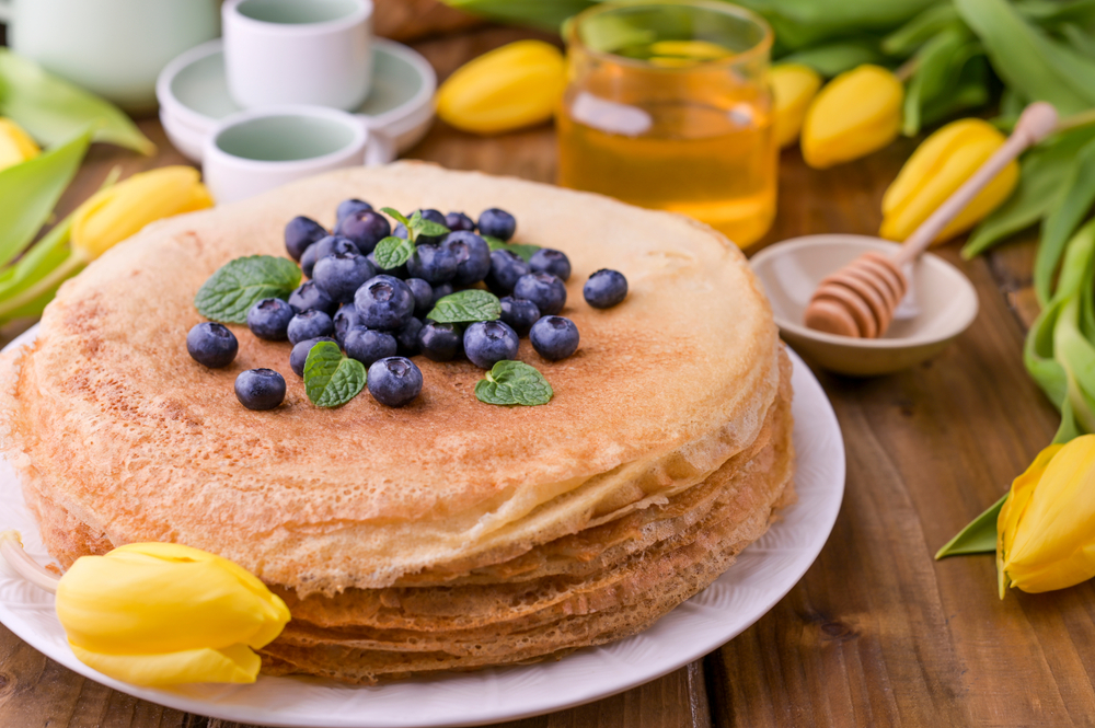 Large pancakes on a plate with blueberries on top and flowers around.