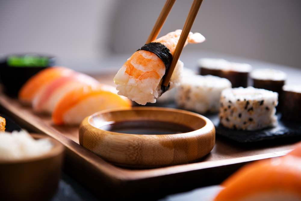 Close up of chopsticks picking up sushi on a wooden plate