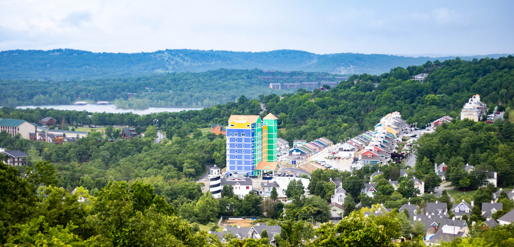 Aerial view of Branson with buildings and green trees on hills in the background.