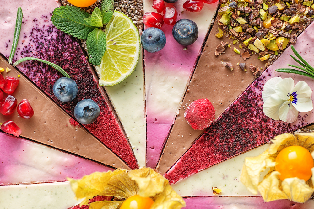 Colorful cheesecakes laid point to point with fruit and edible flowers. 