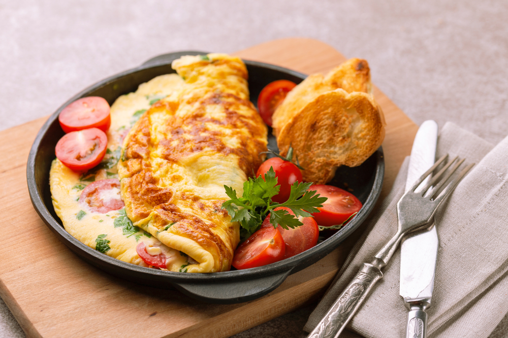 Omelette served in black pan with cherry tomatoes and toast. Silverware and napkin on right in photo. Food in Columbus Ohio.