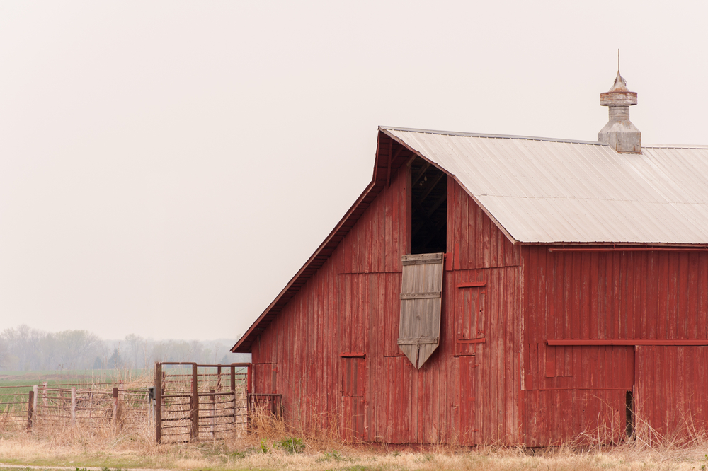 An old red barn on a prairie in Nebraska. There is fog in the air and the sky is very gray. One of the best things to do in Lincoln.