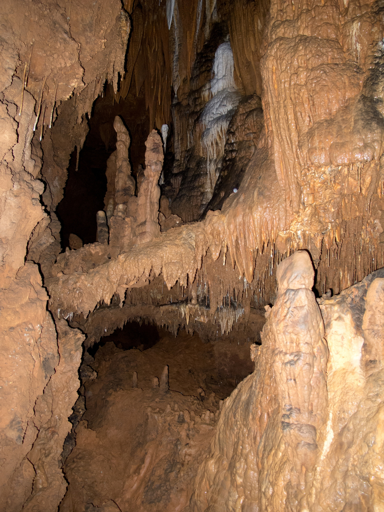 Brown limestone formations in one of the caves on Missouri with some areas illuminated with lights.