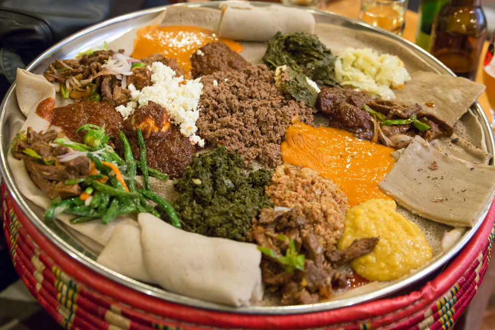 A large platter with a variety of Ethiopian foods like you can find at the Ethiopian restaurants in Lincoln. There is ground meat, cooked greens, sauces, and a type of flatbread.