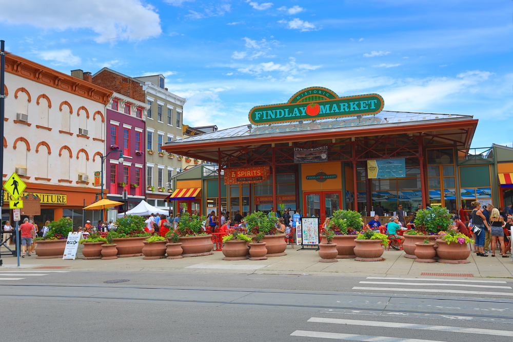 The exterior of Findlay Market, one of the best things to do in Cincinnati. There are large terracotta pots with plants in them at the front. There are people standing around outside. 