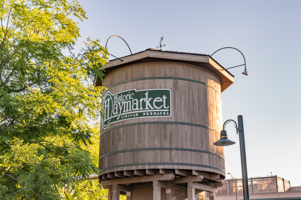 The wooden water tower in the heart of the Historic Haymarket District, one of the best things to do in Lincoln. Next to it is a large tree and a tall light post. 