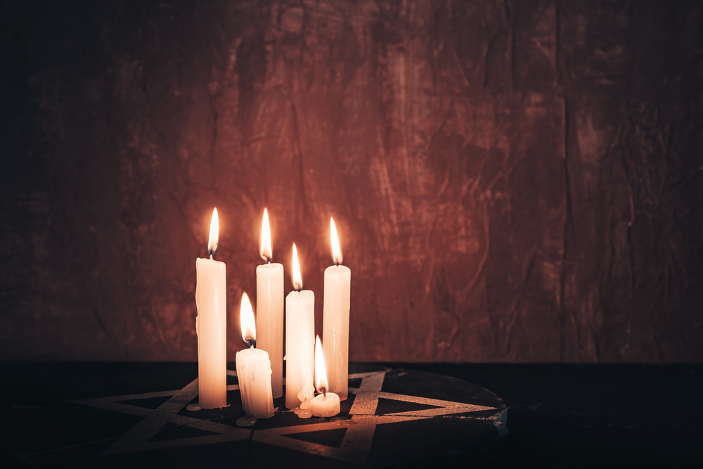 Candles that are lit and nestled into the center of a Star of David. They are next to a wall that marks a Holocaust Memorial. 