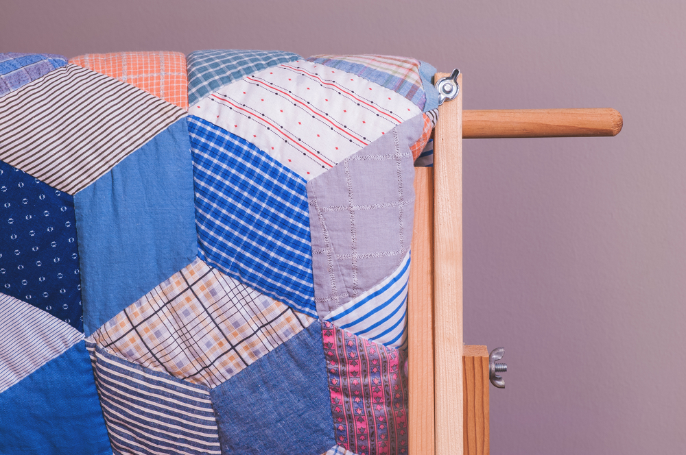 A quilt on display that has fabric with all kinds of patterns in shades of blue, purple, pink, orange, and red. The pieces are cut into trapezoids. 