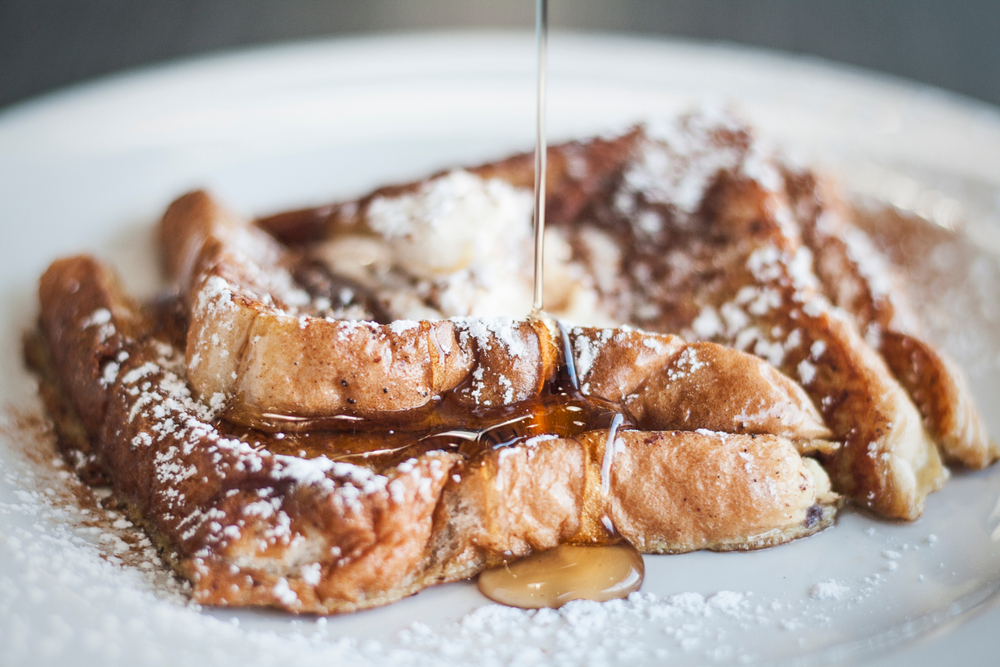 Two slices of French Toast dusted with powder sugar with syrup drizzling over it.  Columbus restaurants.