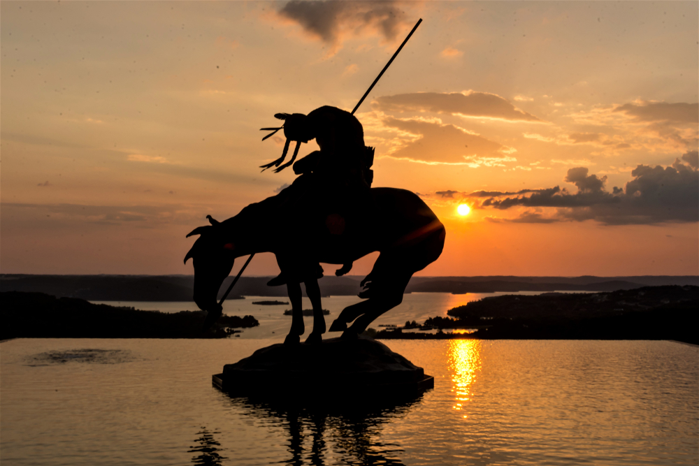 An American Native Indian Staue riding a horse at sunset at top of the hill in Branson