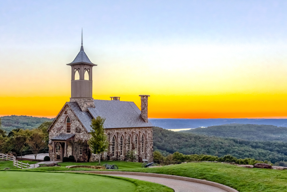 A church at the top of the hill with mountains and sunset in the background