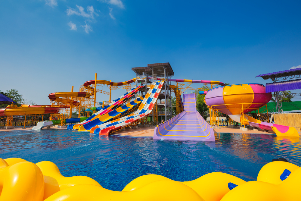 A set of different sized waterslides that go into a large pool at a waterpark. The waterslides are all different colors, some are striped and some are solid. 