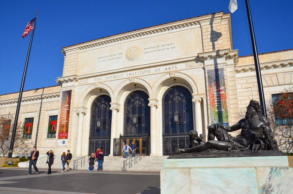 The exterior of the Detroit Institute of Arts. It is an old stone building and in front of it are large steps and bronze sculptures. One of the best Detroit attractions.