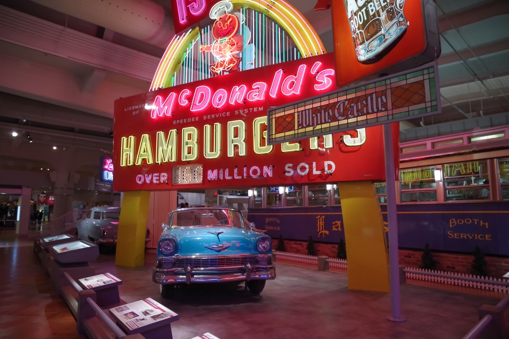 An exhibit at the Henry Ford American Innovation Museum. There is a large McDonalds neon sign, an old Cadillac car, a root beer sign, a stained glass White Castle sign, and tons of other stuff. Its one of the best things to do in Detroit.