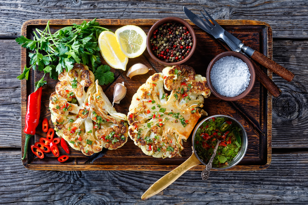 Grilled cauliflower steaks with dressings on a wooden board in an article about restaurants in Duluth