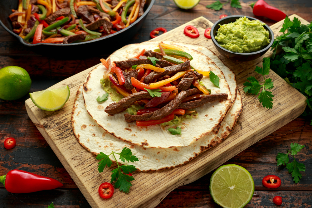 Steak Fajitas on a wooden board with guacamole on the side