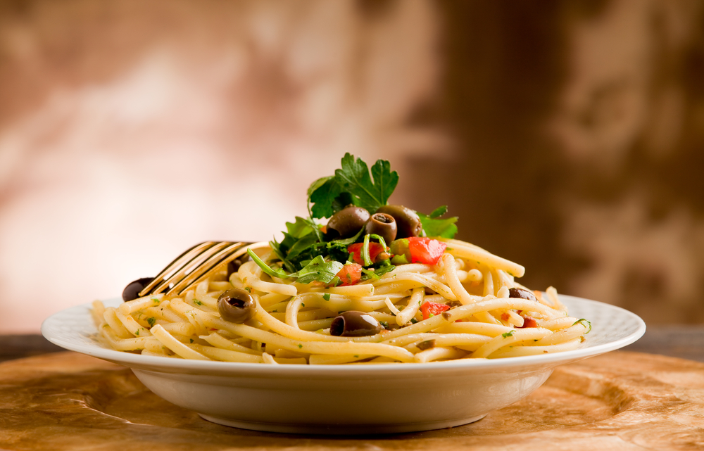 A dish of pasta with olives on top and a fork resting on it.