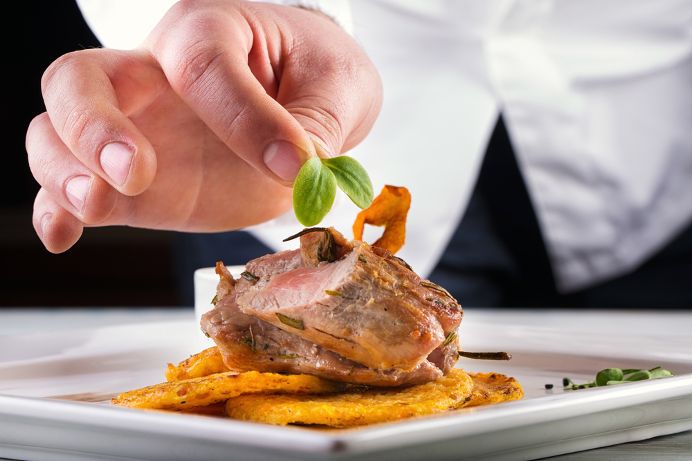 A chef putting a garnish on top of a plate of food containing meat in an article about restaurants in Kansas City