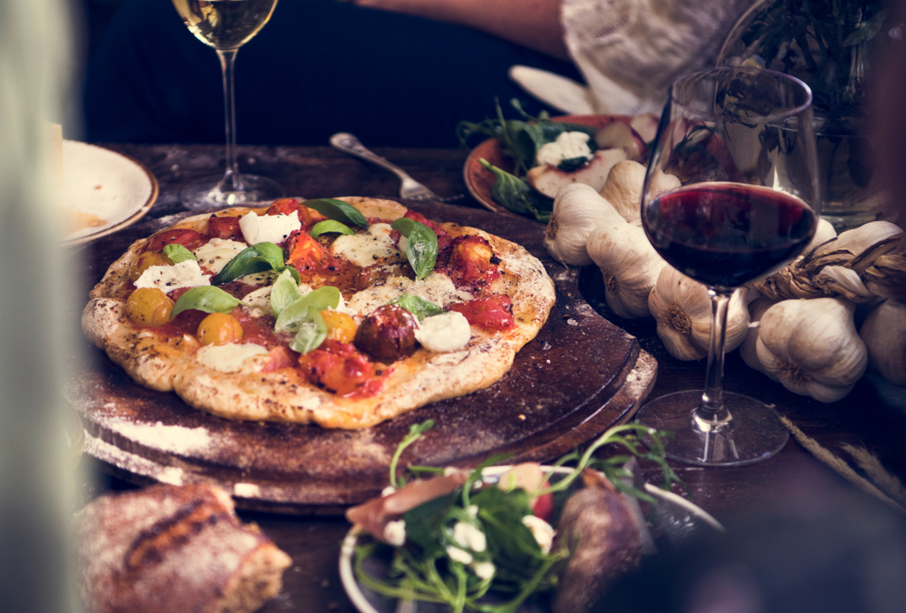 Vegetable pizza on a board on a table with a glass of red wine served at classy KCMO restaurant.