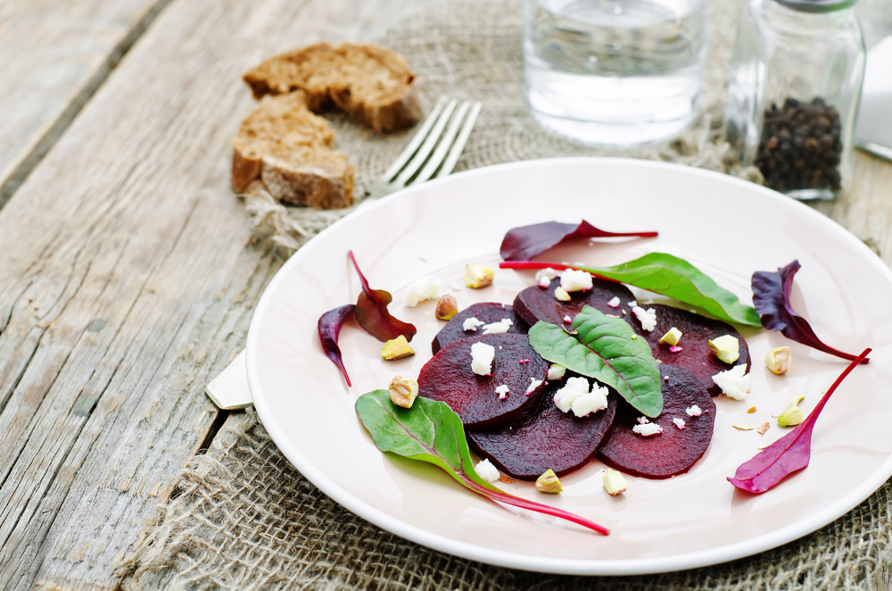 Sliced beetroot on a plate with salad leaves and crumbled cheese