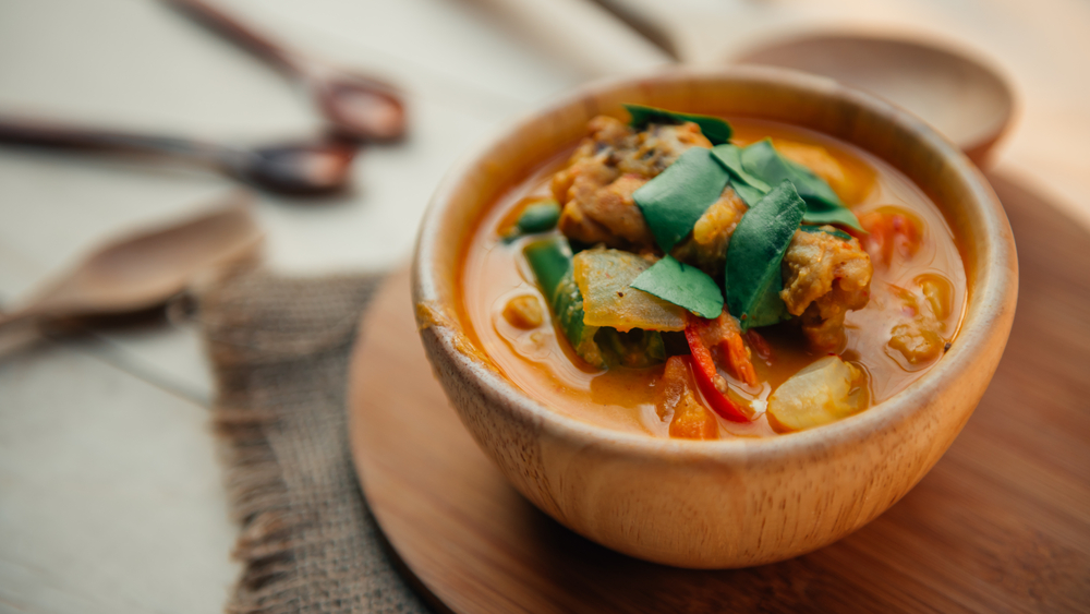 A wooden bowl containing a Thai curry on a table in an article about restaurants in Kansas City