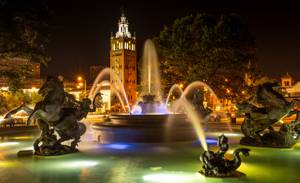 A fountain with statues and a building with a tower in the background in Kansas City