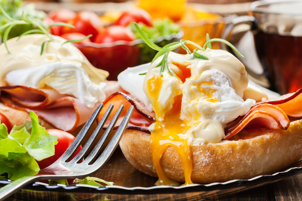 Eggs and bacon on muffins with a fork and egg yolk spilling out