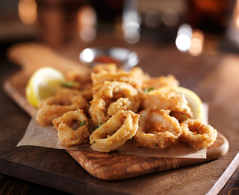 fried calamari rings on a wooden board with a piece of lemon in an article abut restaurants in Minneapolis.