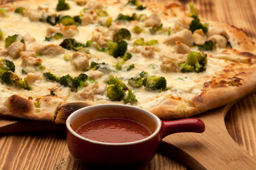 Close up picture of a chicken and broccoli pizza with a pot of sauce in an article about restaurants in Minneapolis