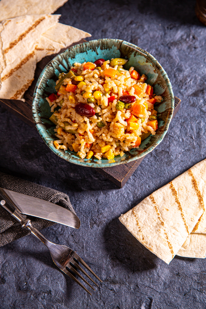 A blue bowl with rice beans and vegetables on a table with cutlery