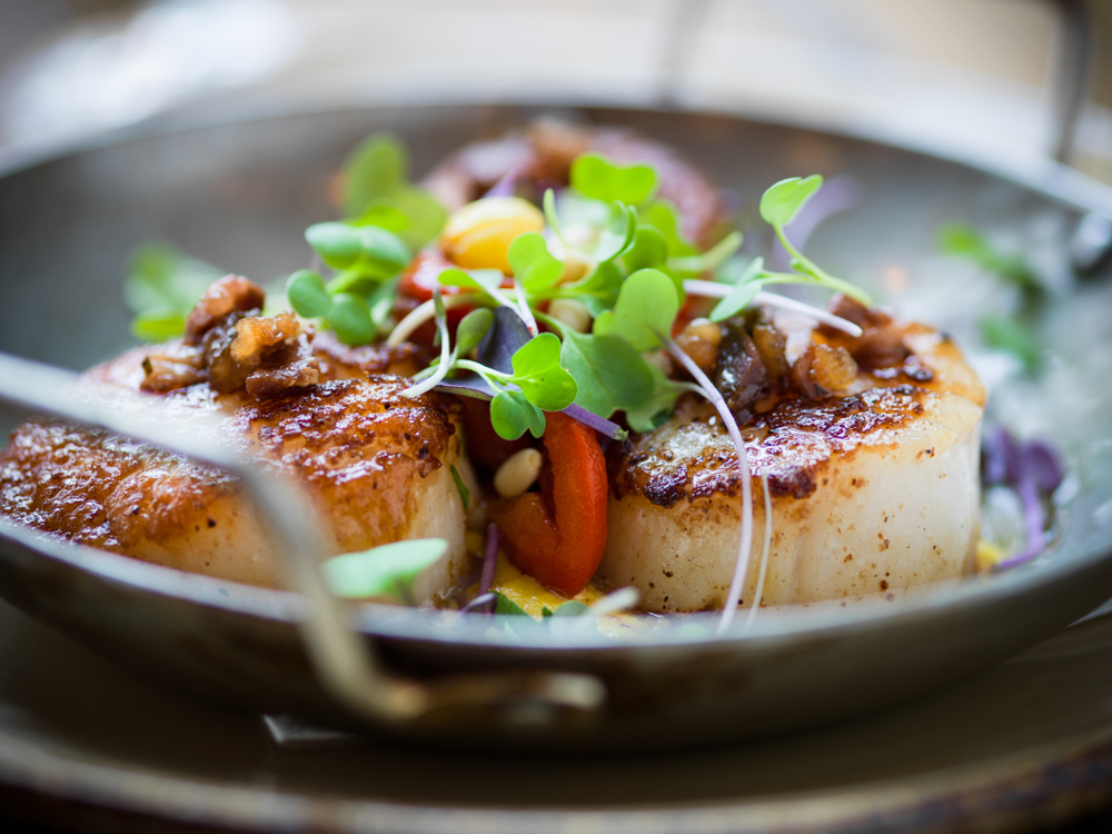 Three seared scallops in a bowl with cress on top in an article about restaurants in Minneapolis