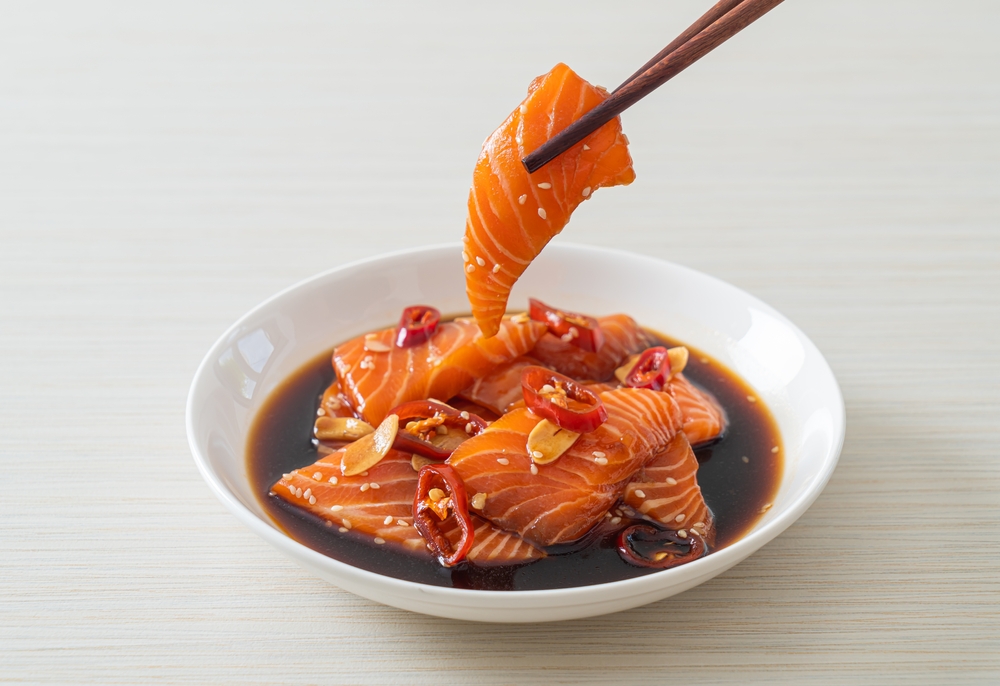 Fresh salmon in a bowl with soy sauce and chopsticks lifting a piece of salmon
