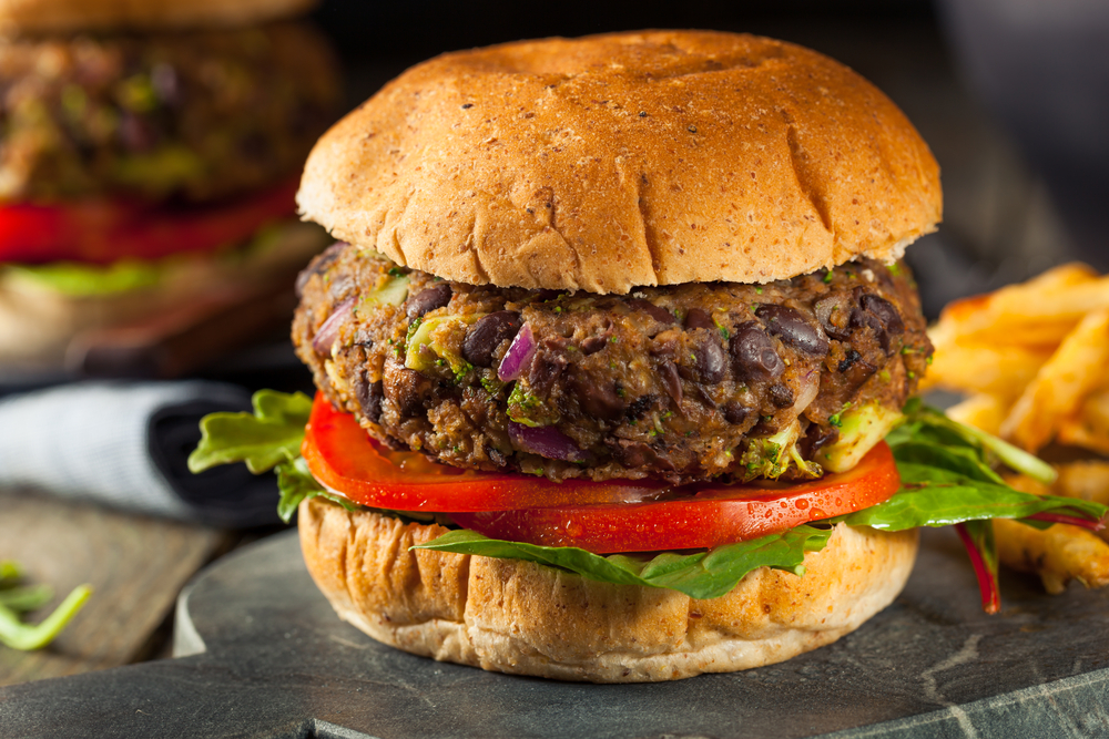 A bean burger in a bun with lettuce and tomatoes on a plate with fries