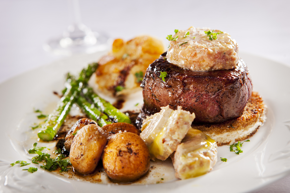 Beef Tournedo on a plate with garlic butter on top and potatoes on the side