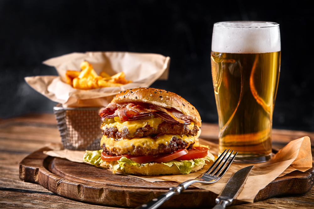 A double cheeseburger with a beer on a wooden board