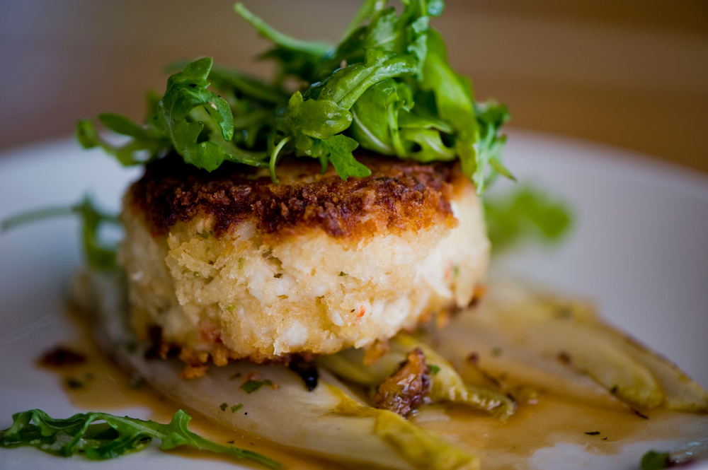 A crab cake on a plate with rocket on top in an article about restaurants in Toledo