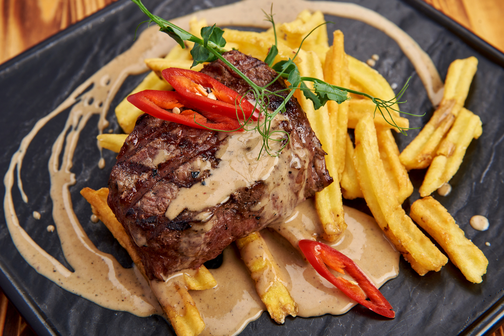 Steak and fried on a grey plate covered with a sauce and chilies