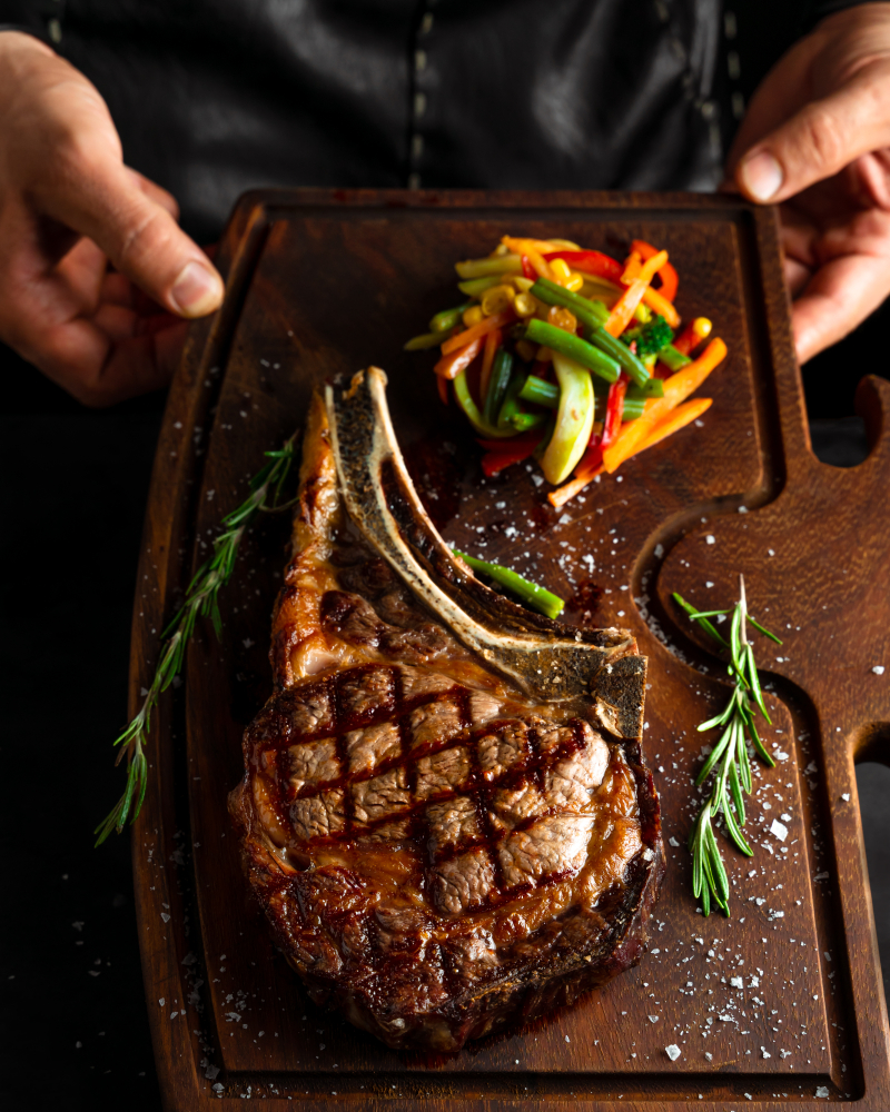 Hands holding a board with a steak on and a side of veg in an article about restaurants in Toledo