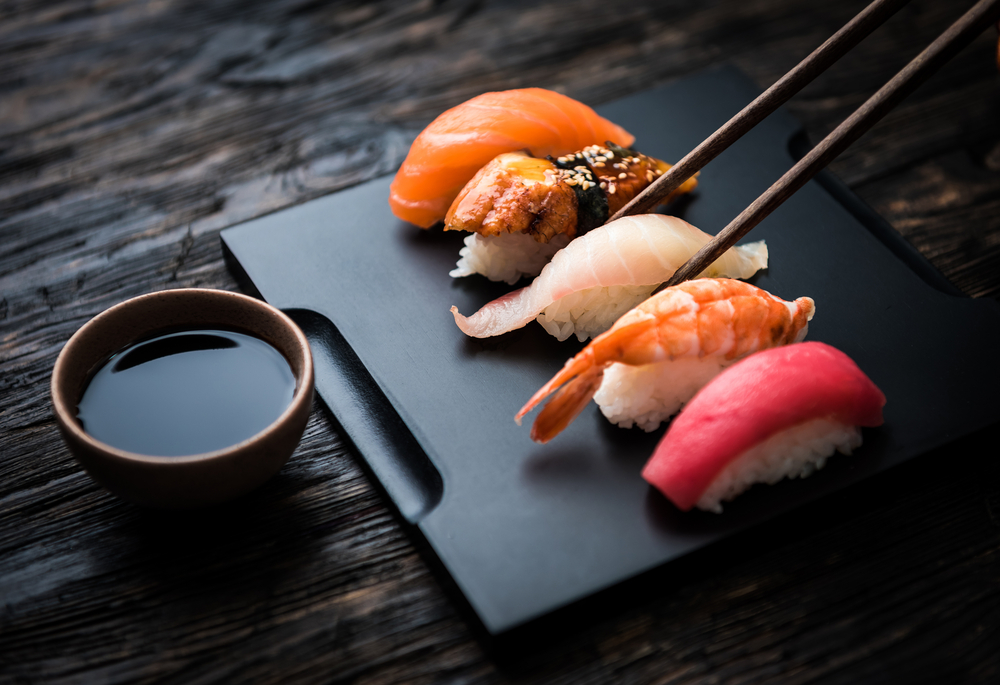 Five pieces of sushi on a slate plate with a dip and chopsticks